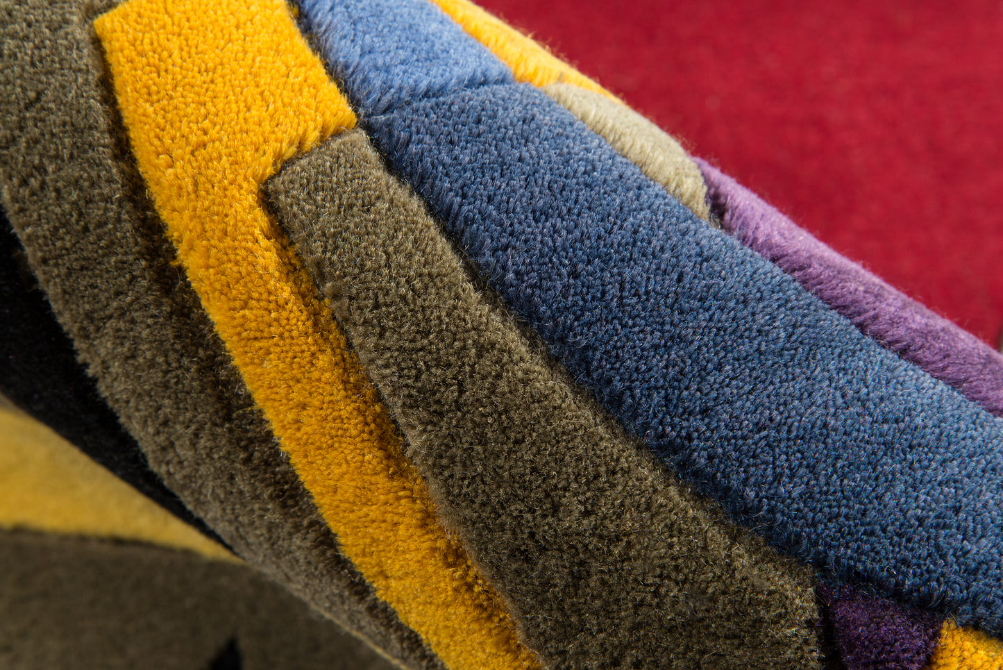 Close-up of multicolor plush fabric strips in yellow, olive, brown, blue and purple, curled in a stacked pile.
