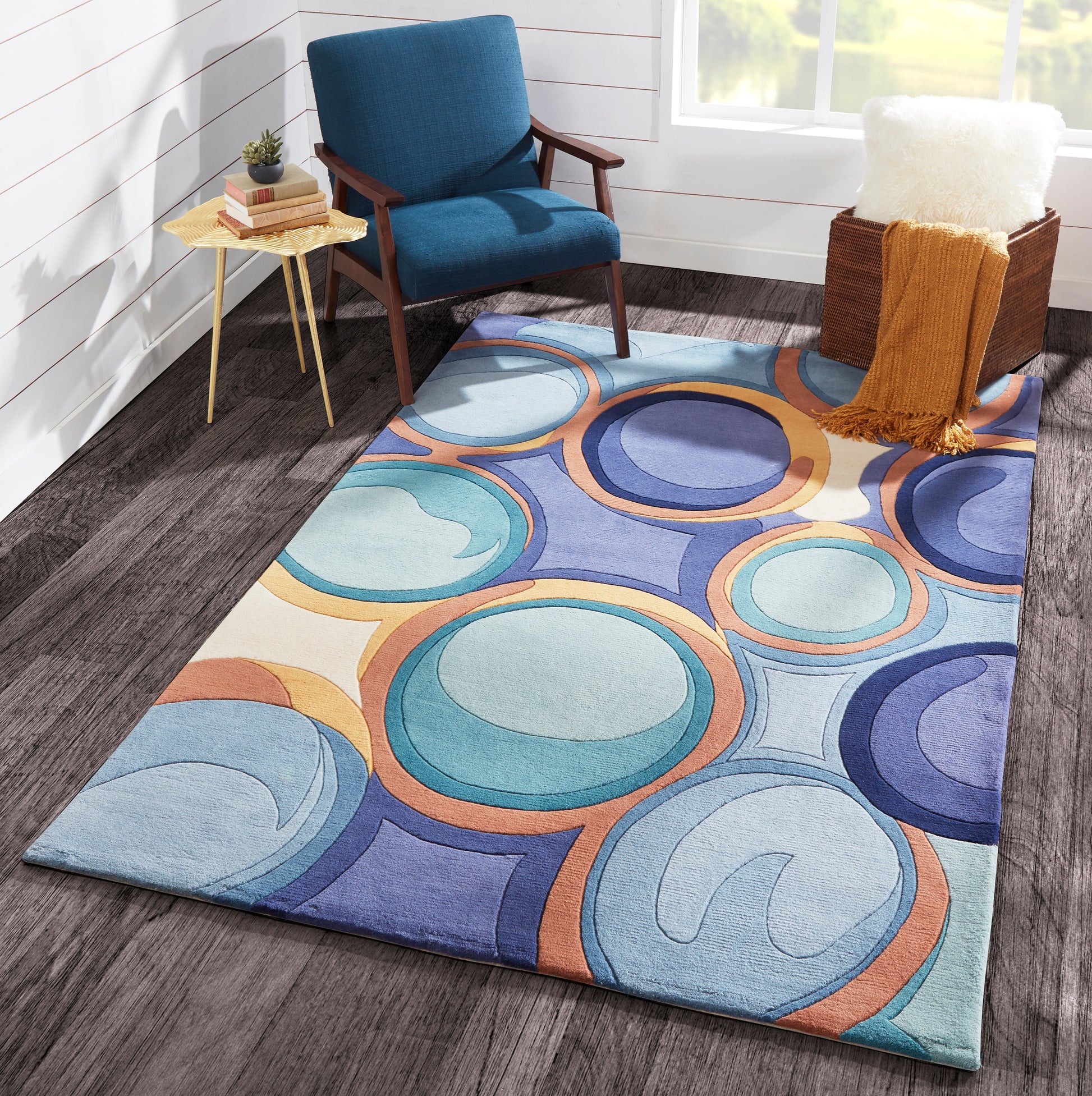 Rectangular plush area rug in blues, teals and orange rings; complements a blue armchair in a modern living room.