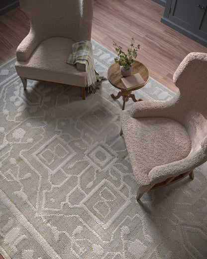 Beige boucle armchairs flank a light blue geometric rug; round wooden table with plant and a book between them.