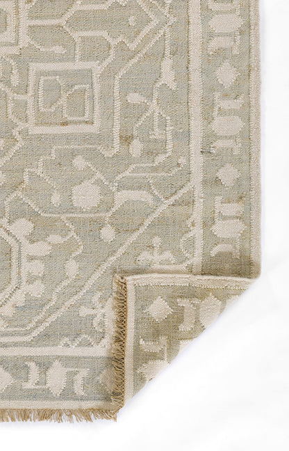 Muted beige and ivory woven rug with geometric/arabesque border, fringe edge and folded corner