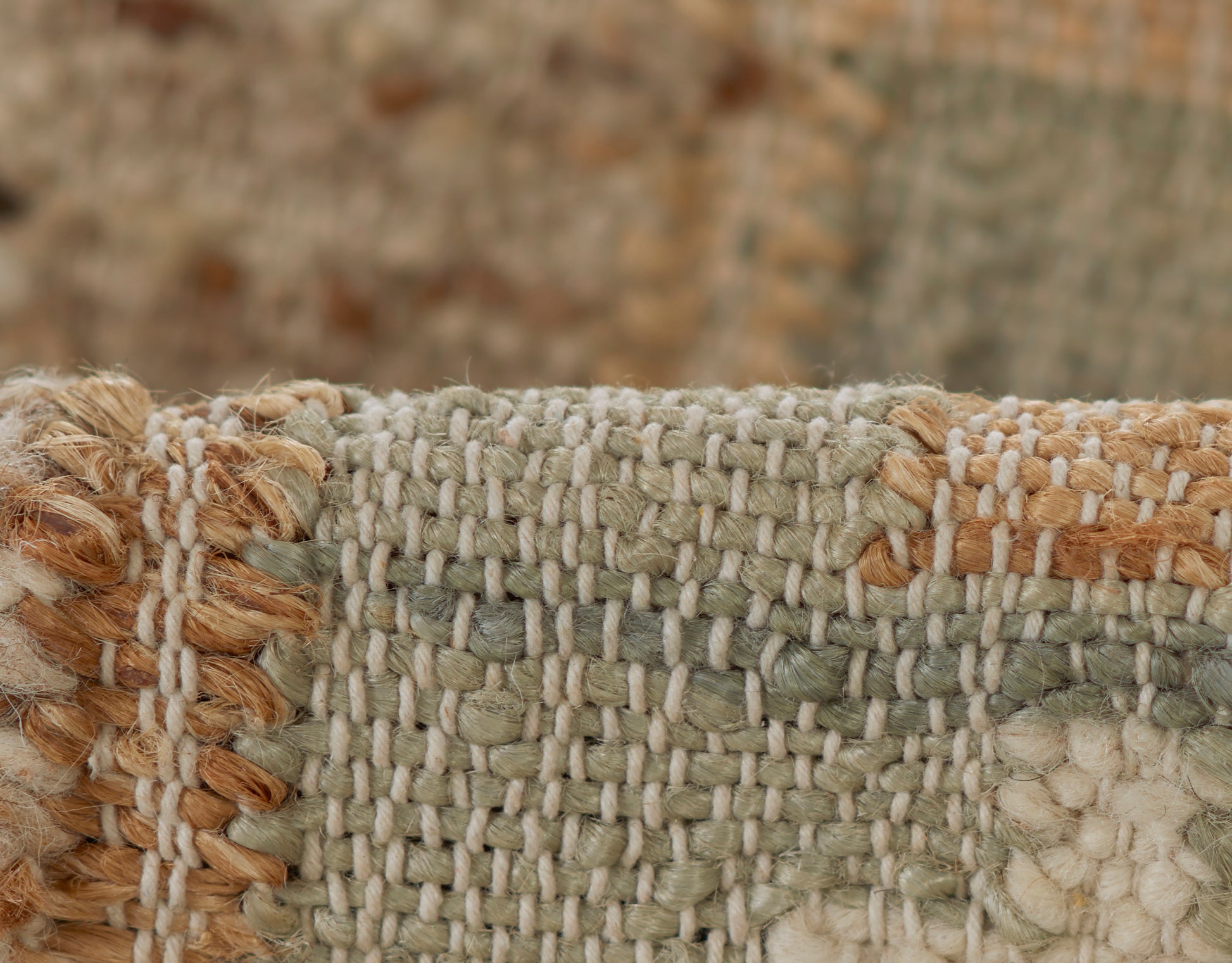 Close-up of a textured woven rug in sage green, ivory and tan with a tan fringe along the left edge.