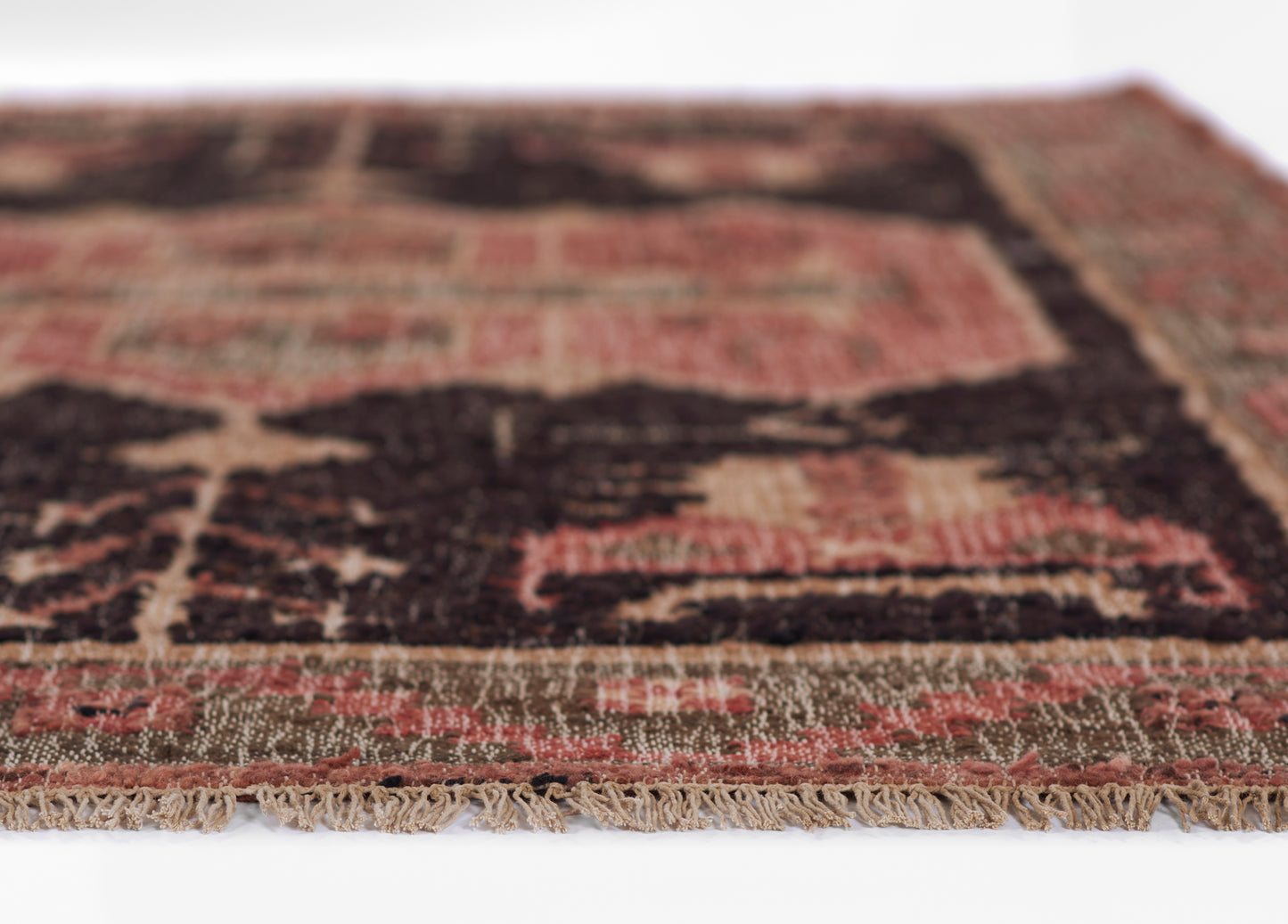 Close-up of a traditional rug in red, dark brown and beige tones with a fringed edge.