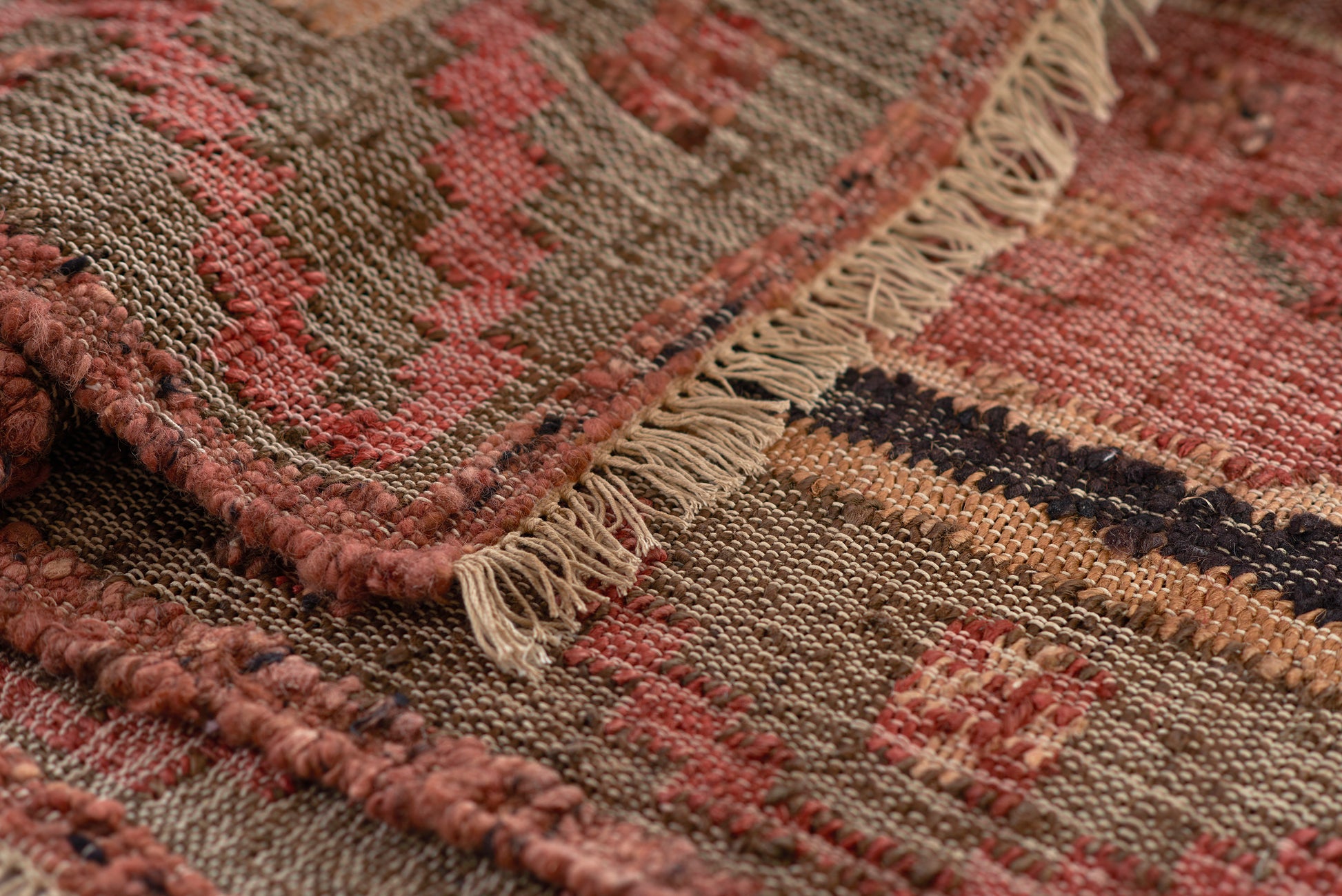 Handwoven kilim rug in red, pink, tan and brown with cream fringe and geometric stripe pattern.