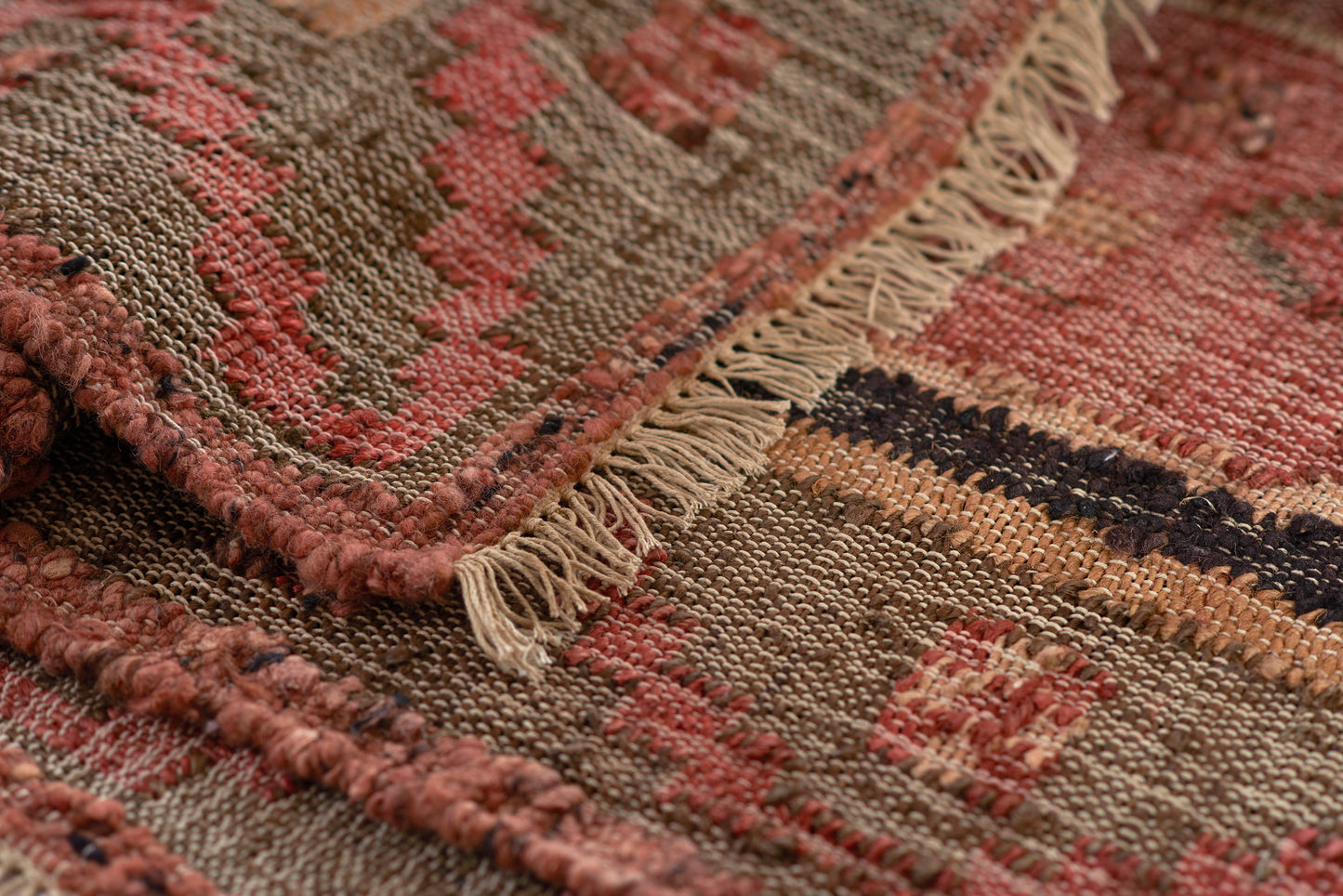 Close-up of a woven kilim rug in red, brown and beige with geometric patterns and fringe.