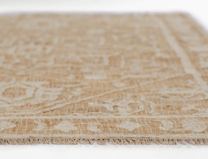 Beige patterned rug with cream fringe along the edge; traditional floral motif and woven texture.