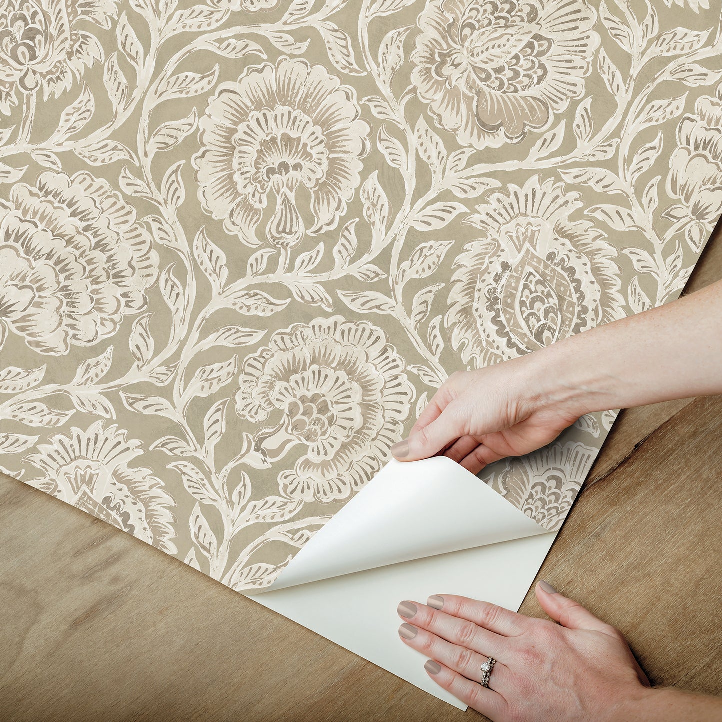Beige damask floral wallpaper peeling back to reveal brown backing, vintage elegant interior wall covering.