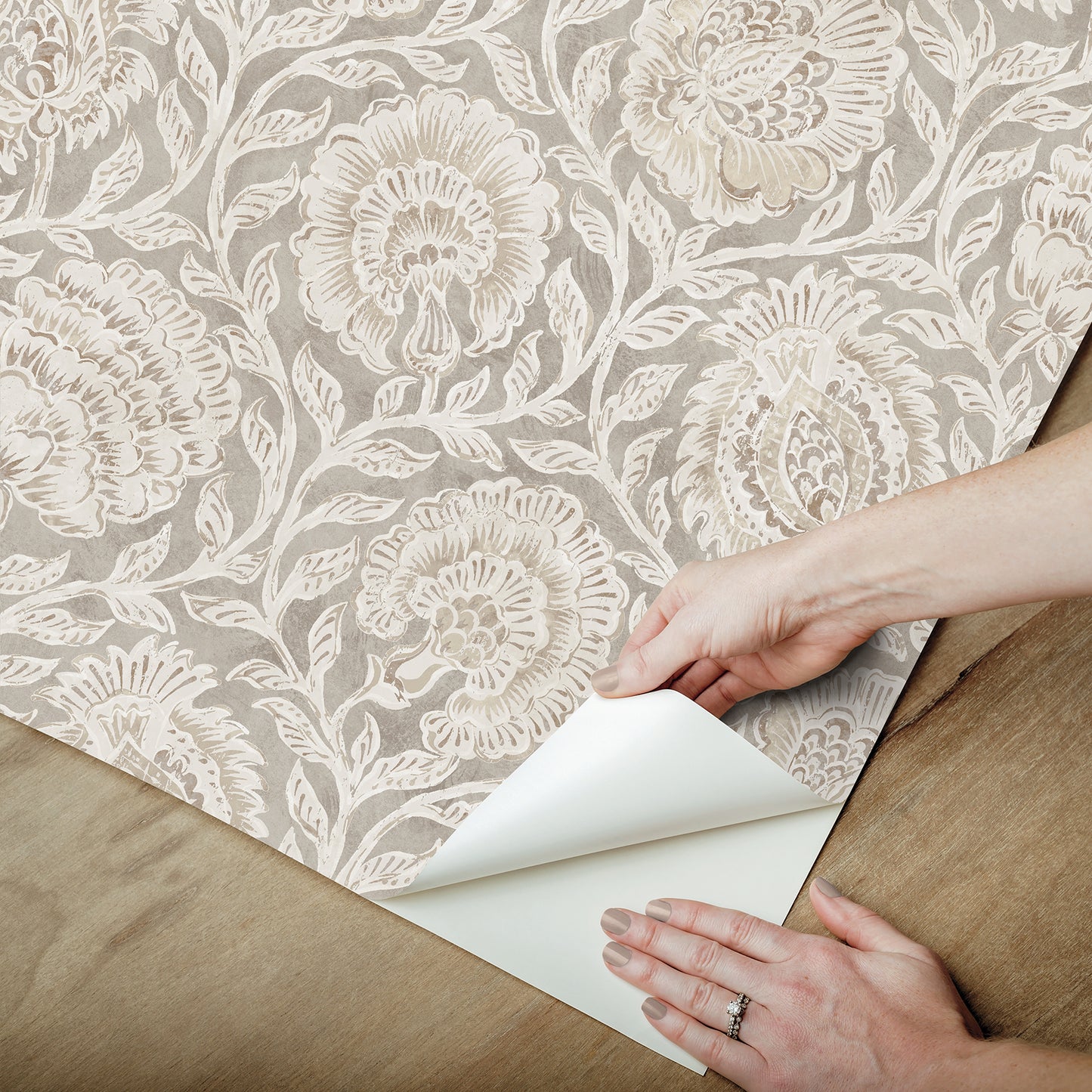 Beige damask wallpaper with ivory floral pattern being peeled back on a wooden floor; vintage elegant interior wall covering.