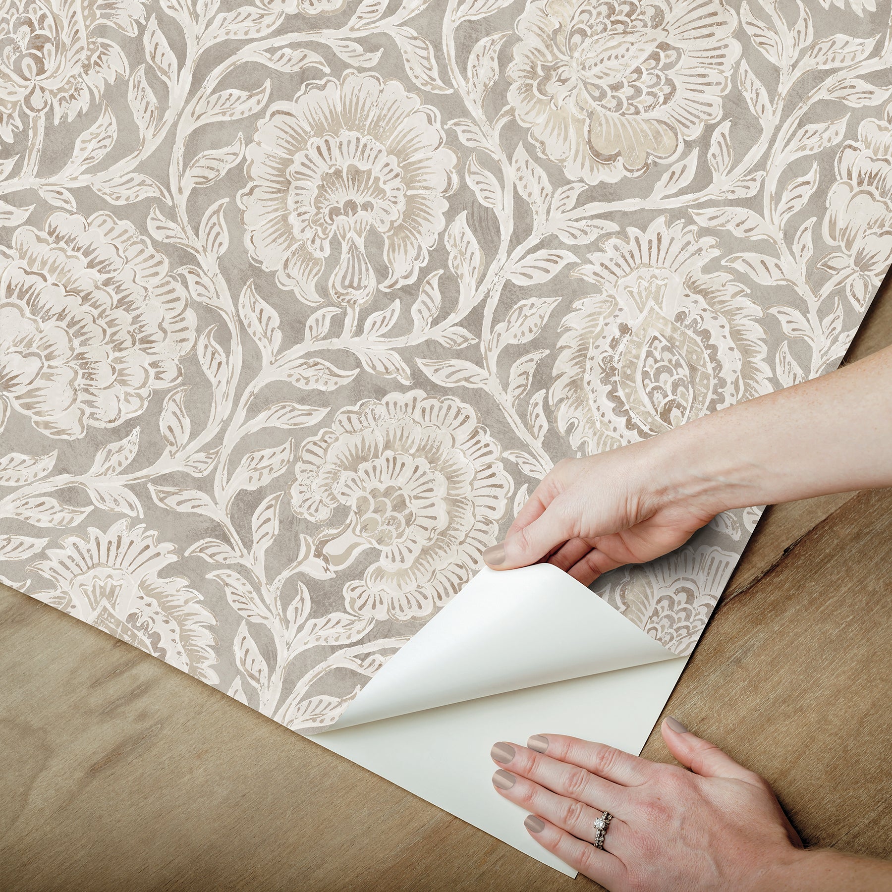 Beige damask wallpaper with ivory floral pattern being peeled back on a wooden floor; vintage elegant interior wall covering.