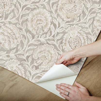 Beige damask wallpaper with ivory floral pattern being peeled back on a wooden floor; vintage elegant interior wall covering.