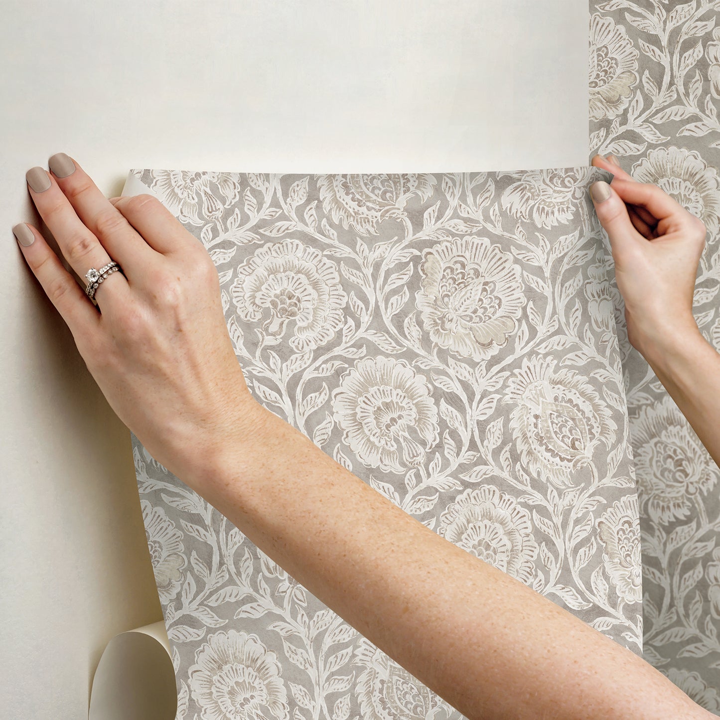Gray damask floral wallpaper swatch with white pattern, held up against a wall.