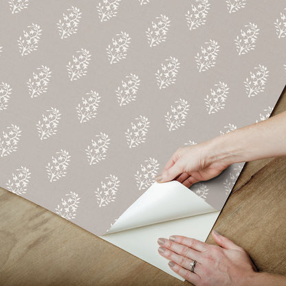 Taupe wrapping paper with white floral pattern being peeled back to reveal white backing on a wooden surface.