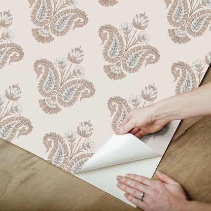 Hands peel back beige damask paisley wallpaper, revealing white backing.