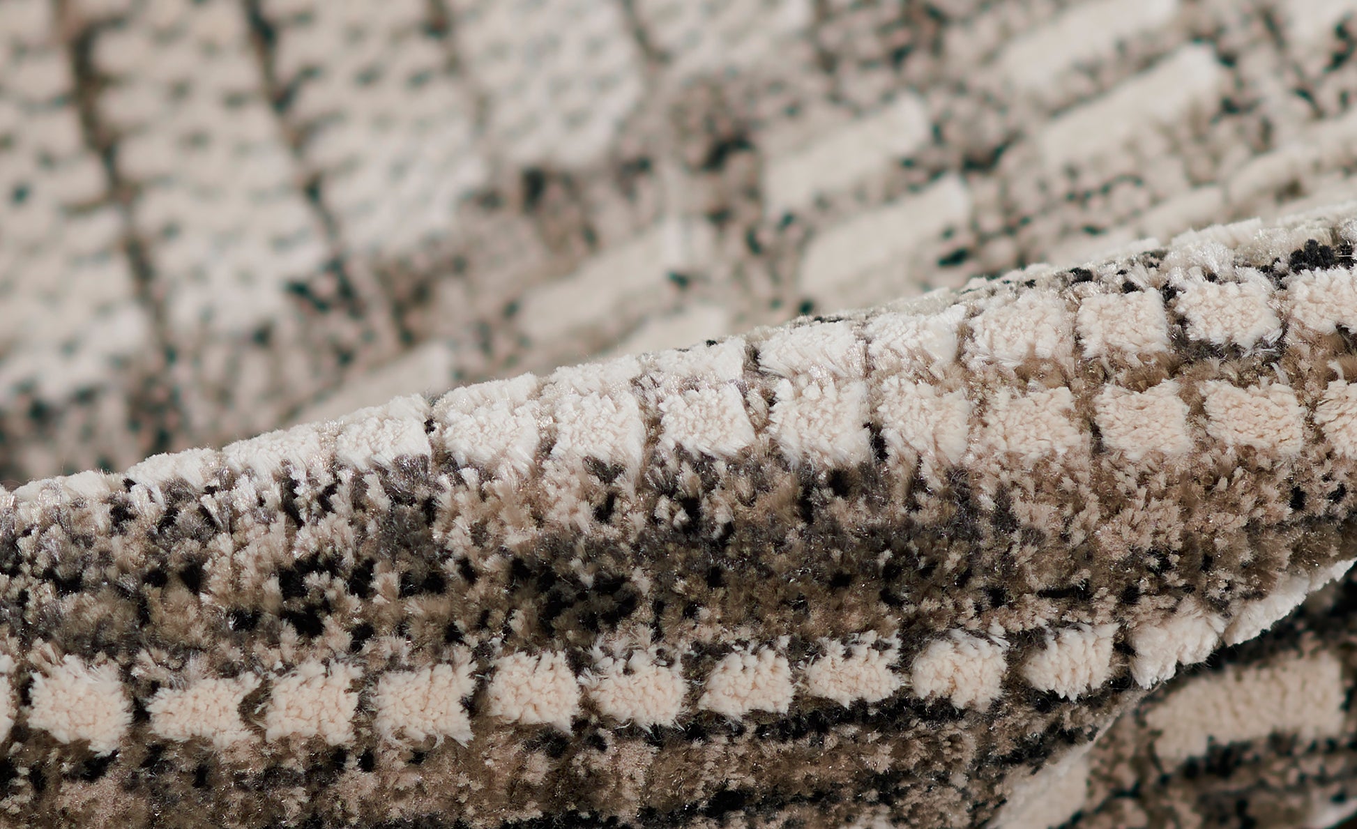 Close-up of a beige & gray shag rug with a plush, looped pile & speckled geometric pattern.