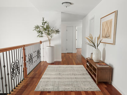 Bright hallway with warm wood floor, black iron railing, tall white planter, gray rug, wooden console with vase.