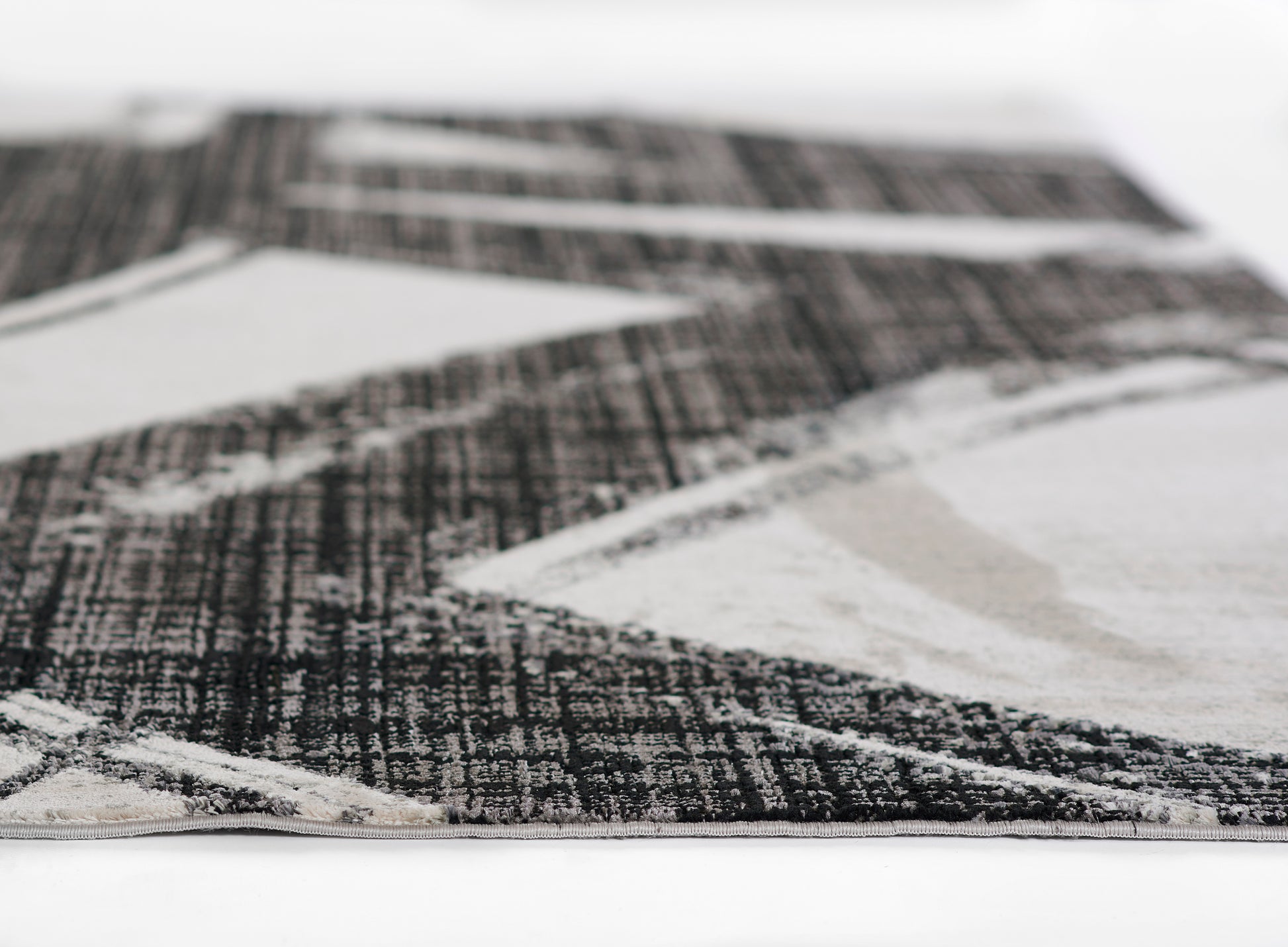 Modern geometric area rug in black, white and gray with triangle pattern; woven low-pile texture and pale edge binding.
