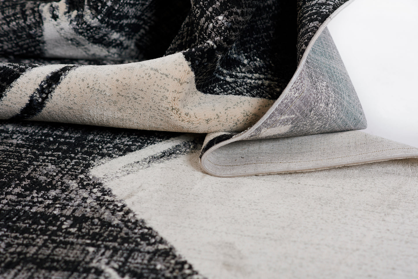 Black and ivory woven rug with abstract pattern; rolled corner reveals light gray underside.