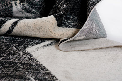 Black and ivory woven rug with abstract pattern; folded edge shows light gray backing.