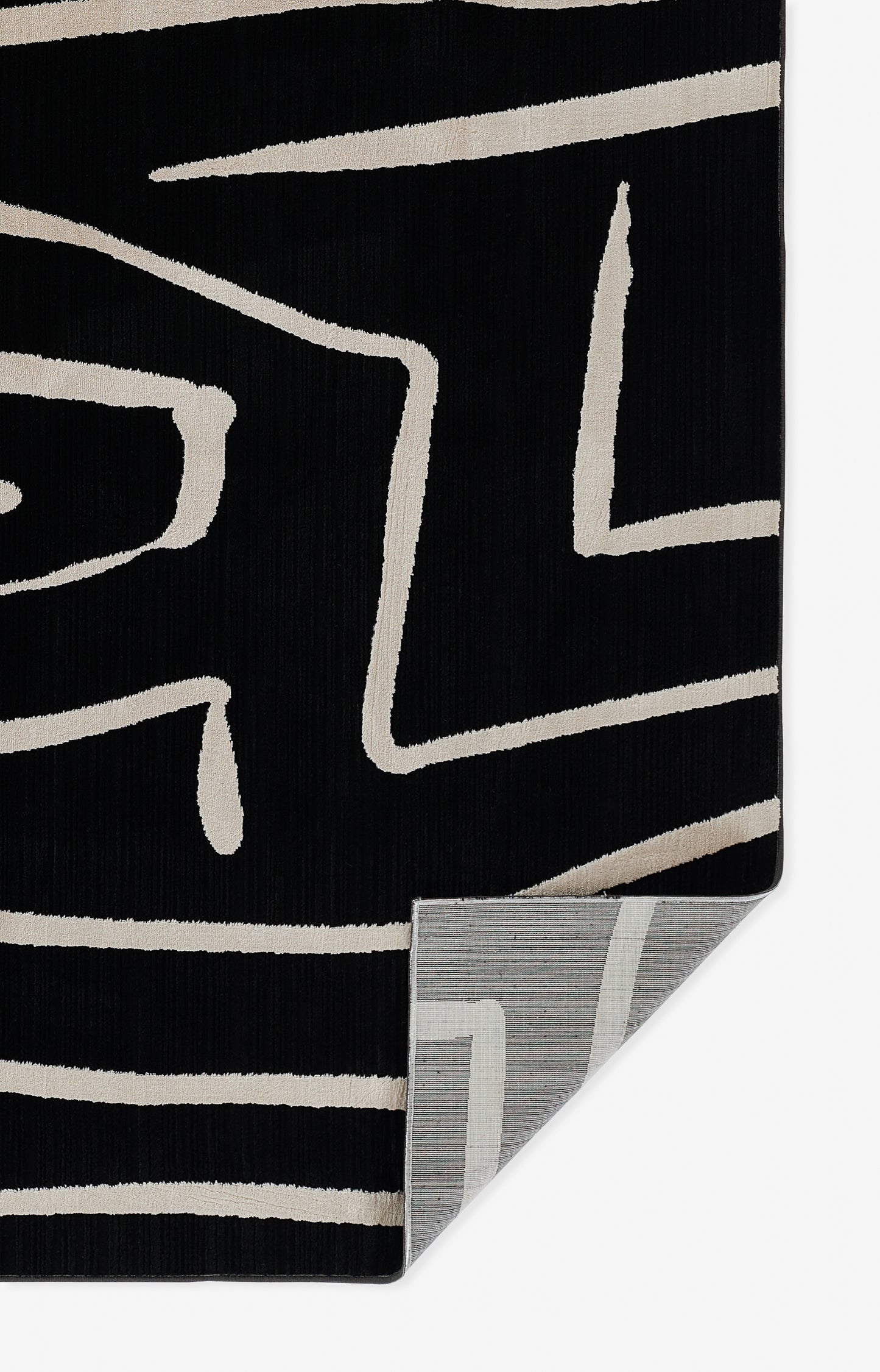 Black rug with beige abstract linear pattern, ribbed texture, folded corner reveals light grey backing.
