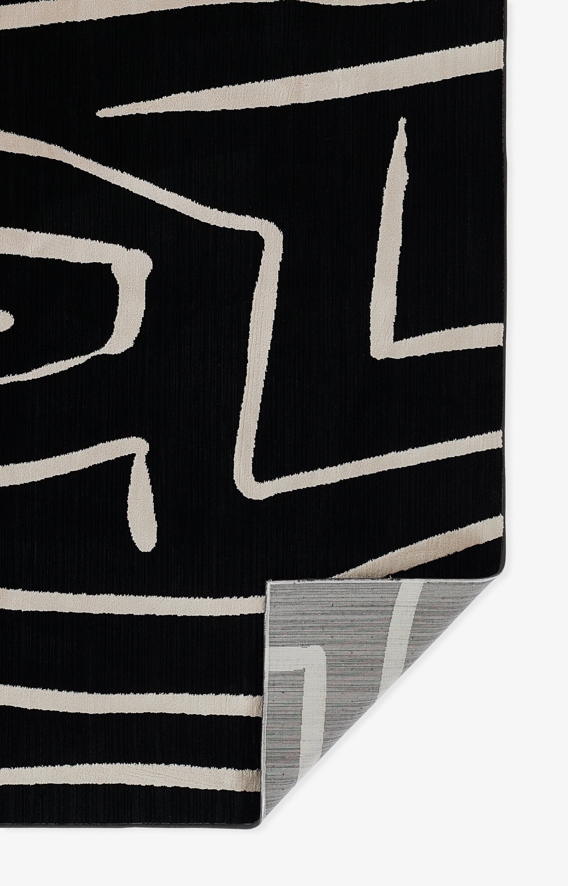 Black rug with beige abstract geometric lines; folded corner reveals grey backing.