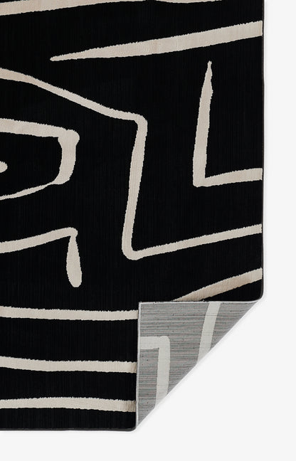 Black rug with beige abstract geometric lines, soft pile; folded corner shows gray striped reverse.