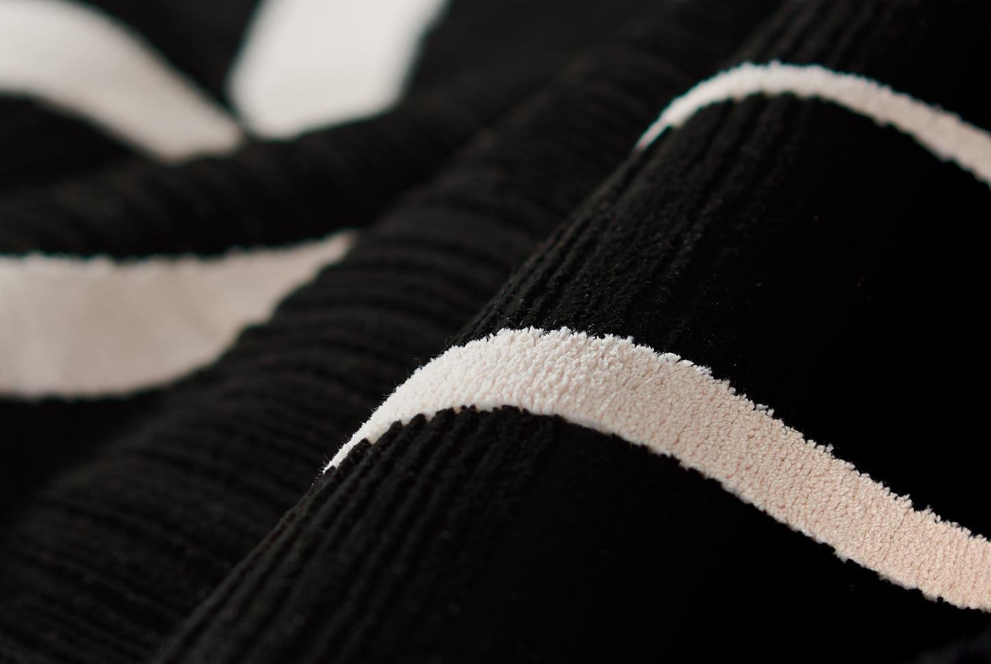 Close-up of black ribbed knit fabric with a beige cream stripe, cozy sweater detail.