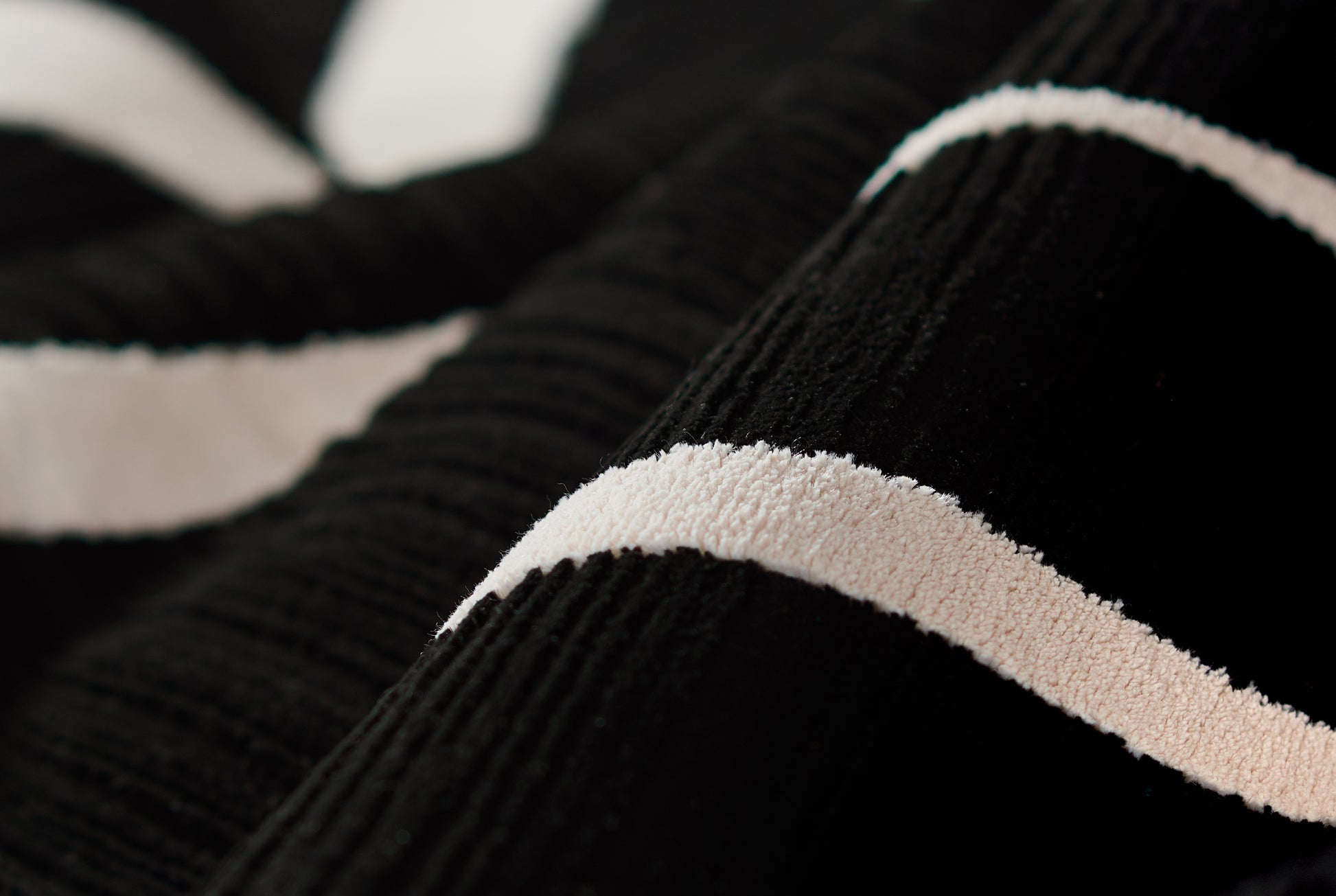 Close-up of a black rug with a ribbed texture and a beige textured stripe.
