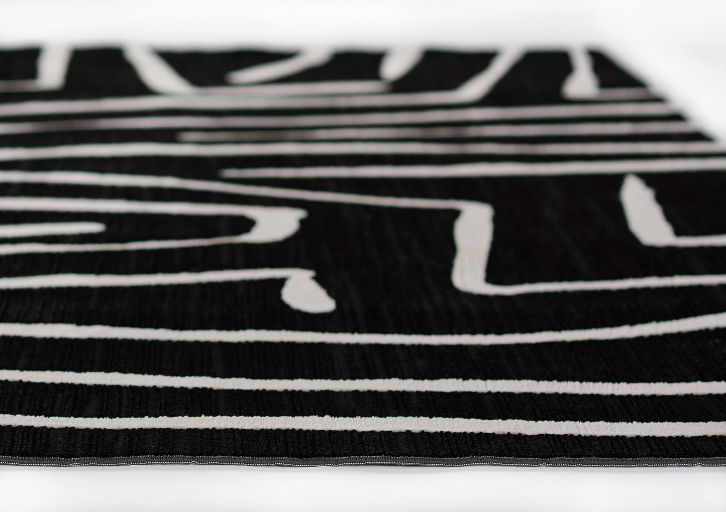 Close-up of black rug with white linear stripes and woven texture; modern abstract floor covering.