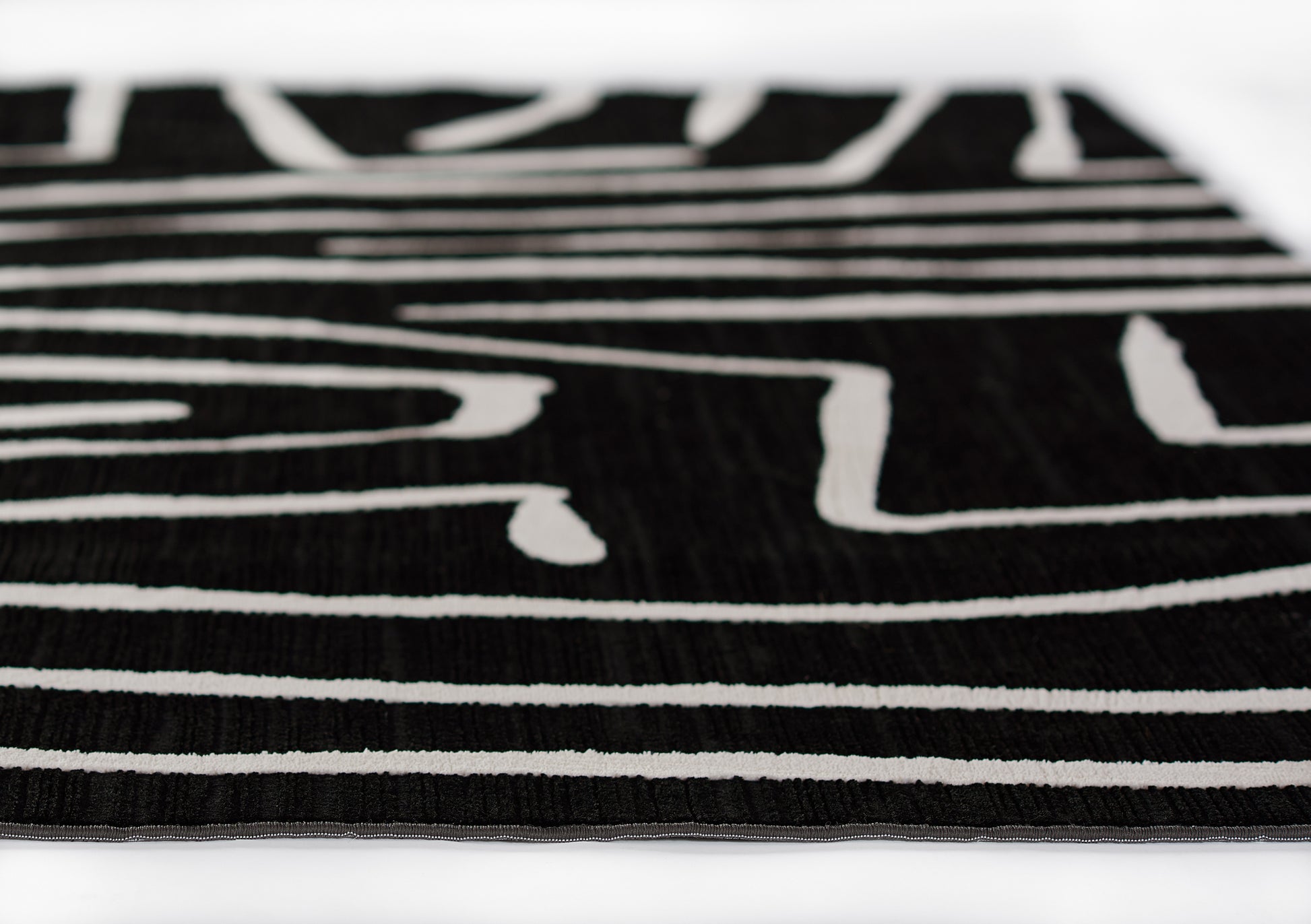Close-up of black rug with white geometric stripes, woven texture and slim edge border.