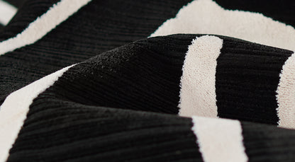 Close-up of black plush fabric with wide off-white stripes; soft terry texture & modern striped throw blanket or towel.