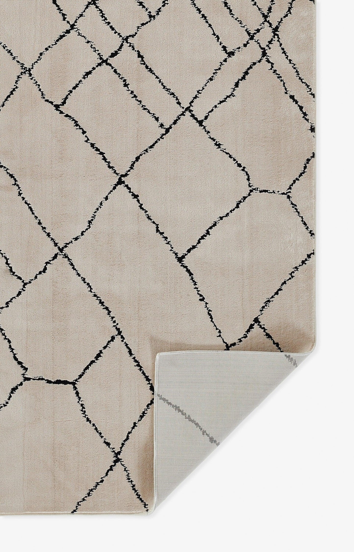 Beige rug with a black geometric lattice pattern, soft pile; folded corner reveals light gray underside.
