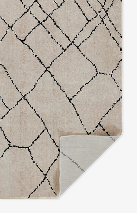 Beige rug with bold black diamond lattice pattern; soft pile, folded corner shows light gray underside.