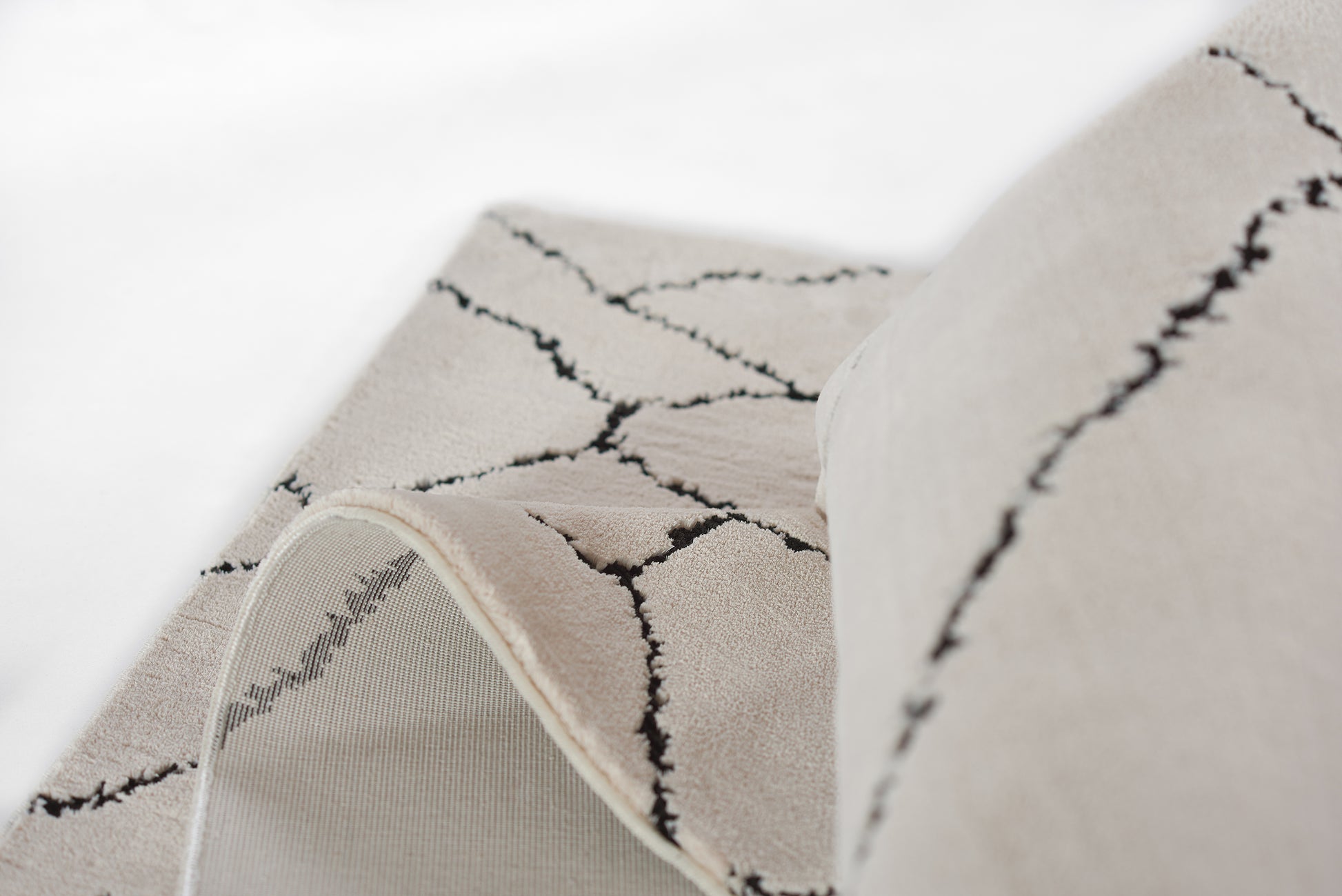 Ivory-beige rug with black crackle geometric lines, soft pile, rolled edge showing underside.