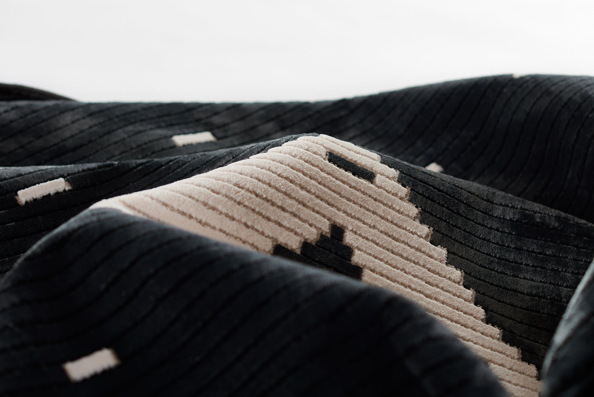 Close-up of black ribbed textile with beige geometric stripe featuring black squares; plush corduroy weave.