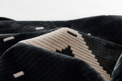 Close-up of black ribbed textile with beige geometric stripe featuring black squares; plush corduroy weave.