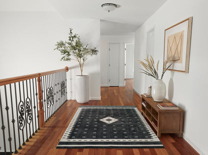 Hallway with black & white geometric runner rug, wooden railing, tall plant, wooden console with vase & dried grasses.