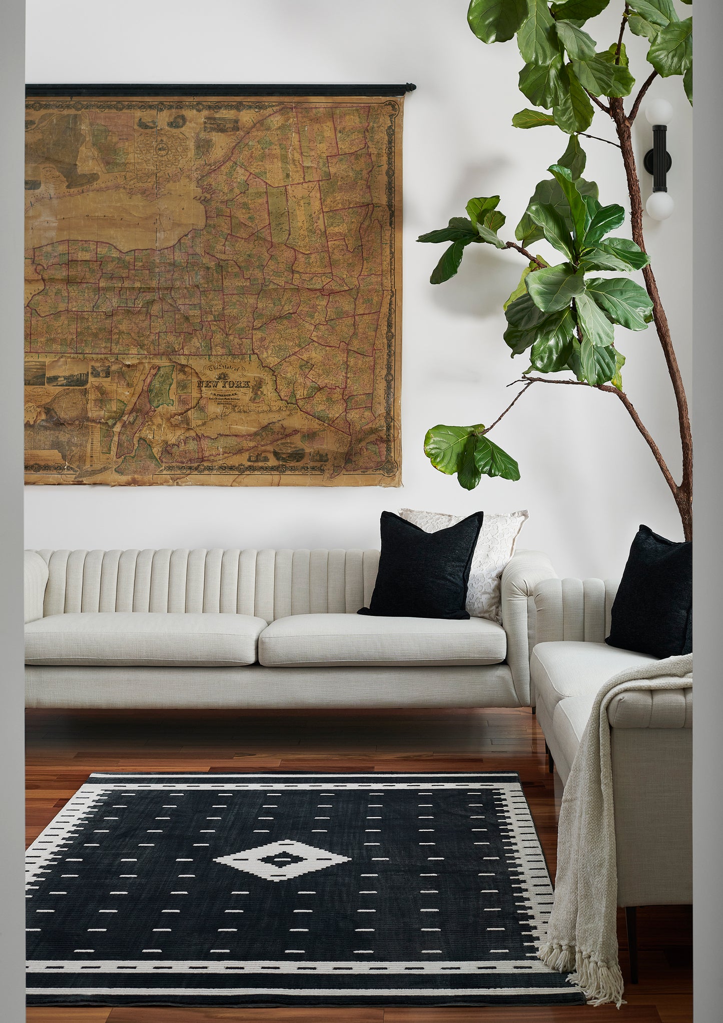 Living room with cream tufted sofa, vintage map wall art, tall plant, and a black-and-white geometric rug.