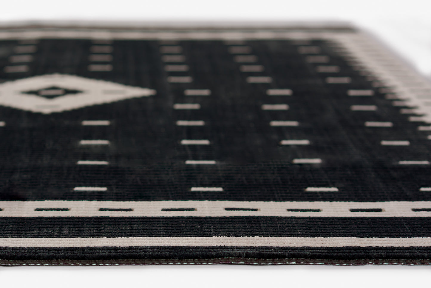 Black woven rug with white geometric border and diamond motif; modern flat-weave.