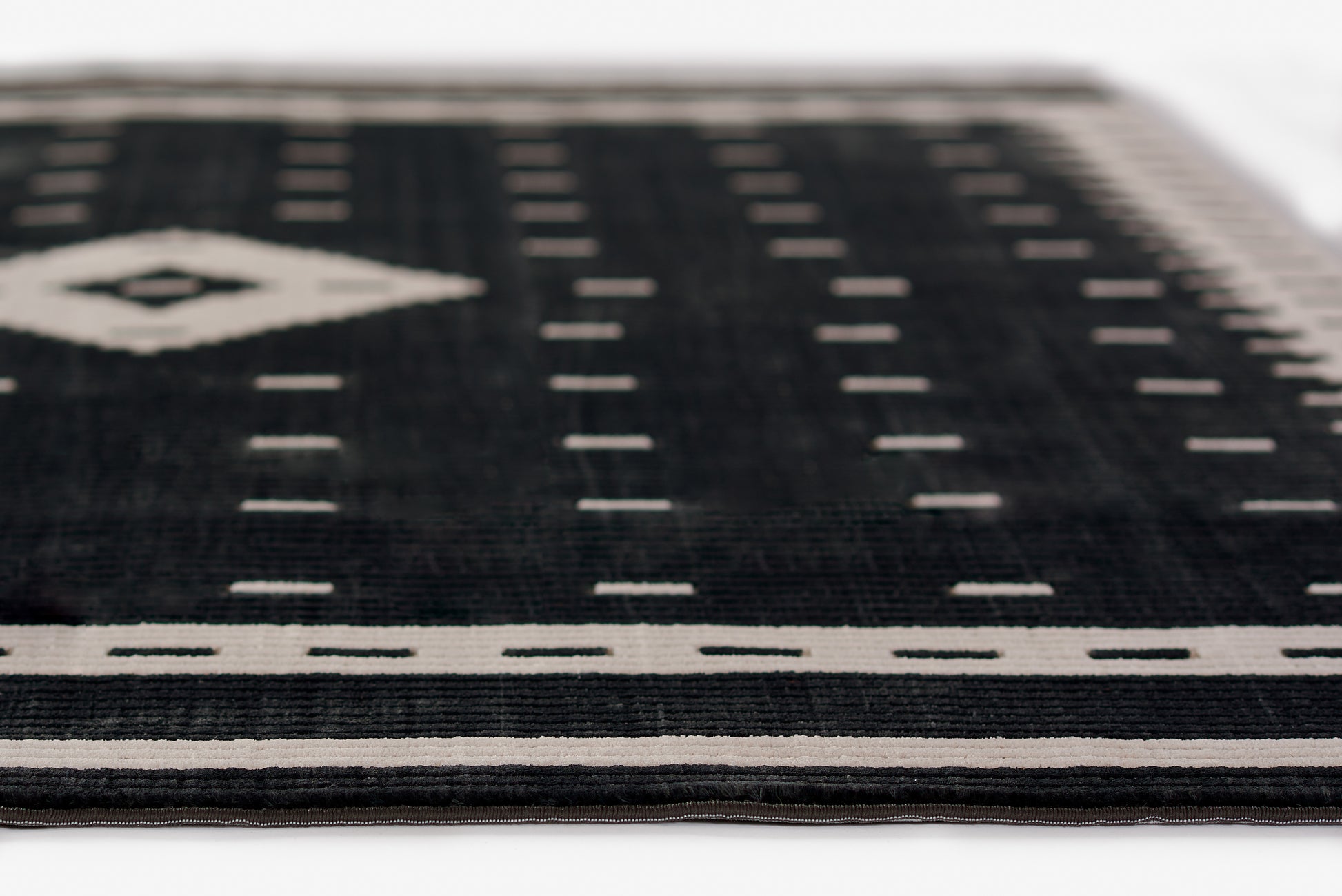 Black woven rug with white geometric border and diamond motif; modern flat-weave.