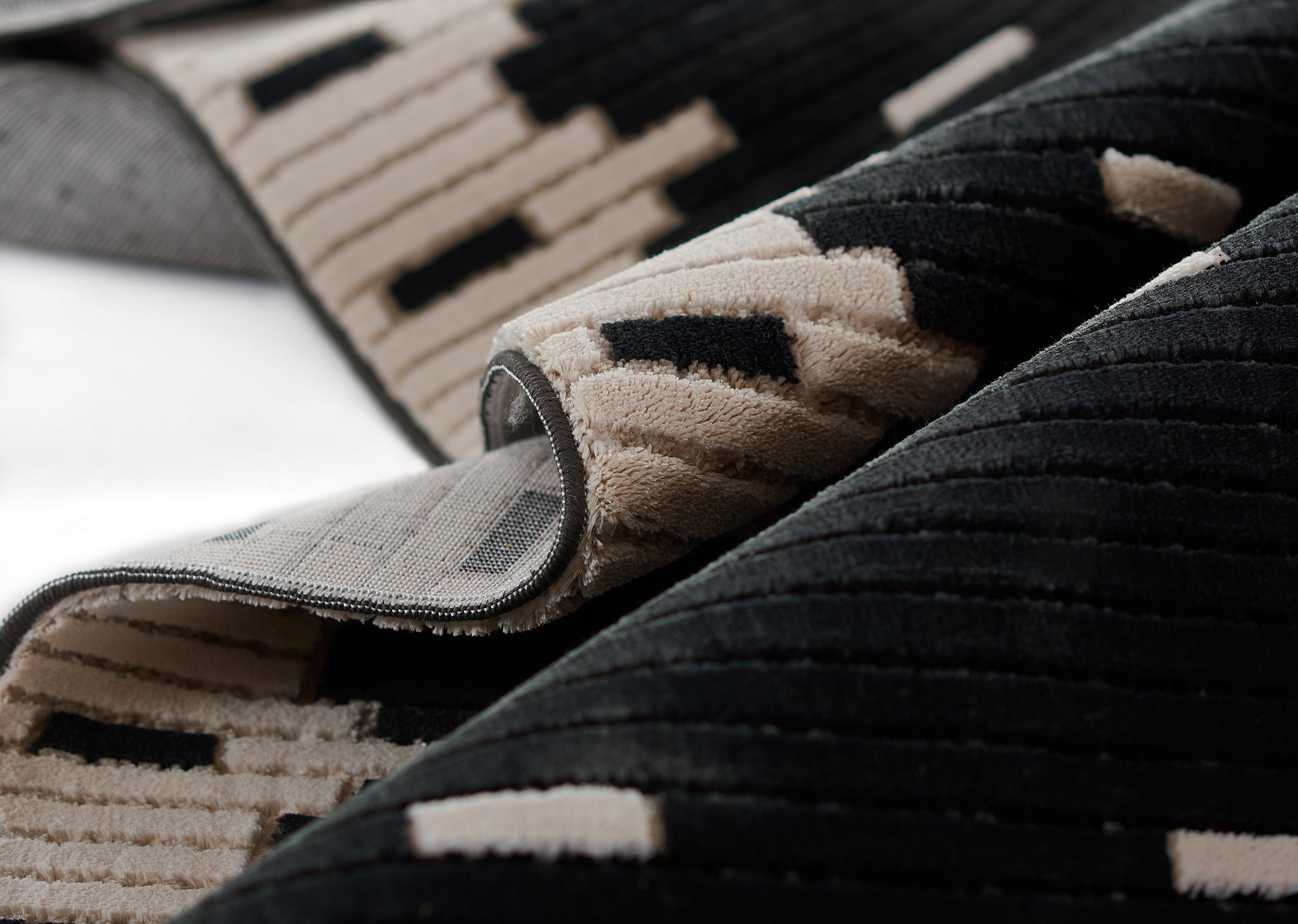Geometric beige and black shag rug, plush pile with rectangular pattern; rolled edge reveals grey backing.