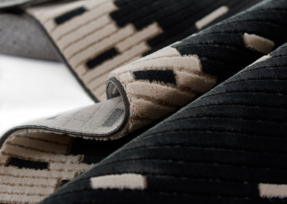 Geometric black and beige plush rug, modern style, rolled to show soft pile and gray checked underside.