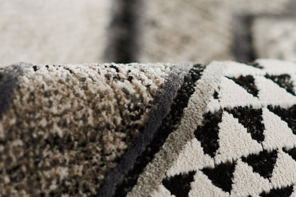 Close-up of plush rug with ivory base and black geometric triangles; thick pile and folded edge visible.