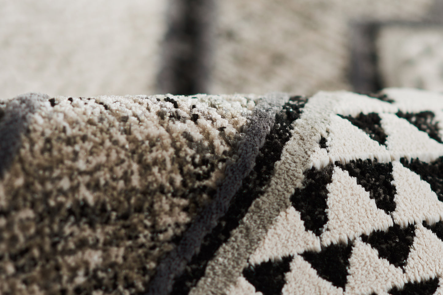 Close-up of a plush geometric rug in ivory, black and gray with triangular pattern and dark edge trim.