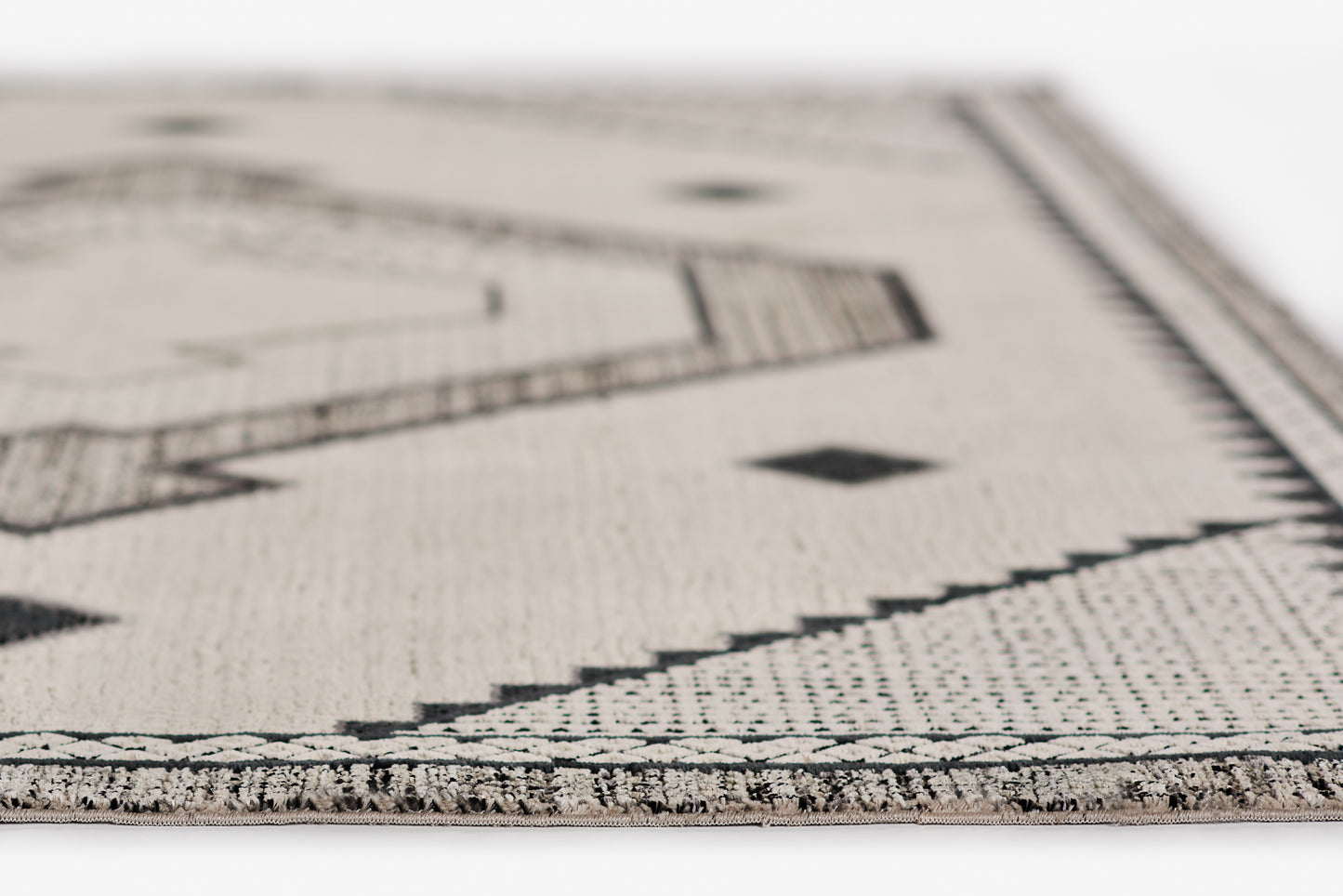 Ivory woven rug with black geometric motifs, zigzag border, fringe edge, boho style.