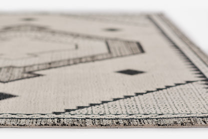Ivory woven rug with black geometric motifs, zigzag border, fringe edge, boho style.
