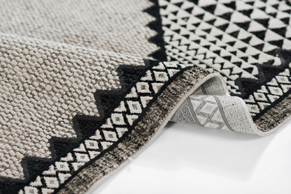 Beige ivory and black geometric area rug with diamond border; textured woven pile and a folded corner exposing the backing.