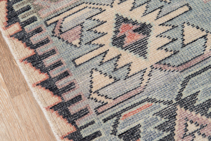 Nomad blue rug with geometric triangles and zigzag border in beige, pink and navy on wood floor.