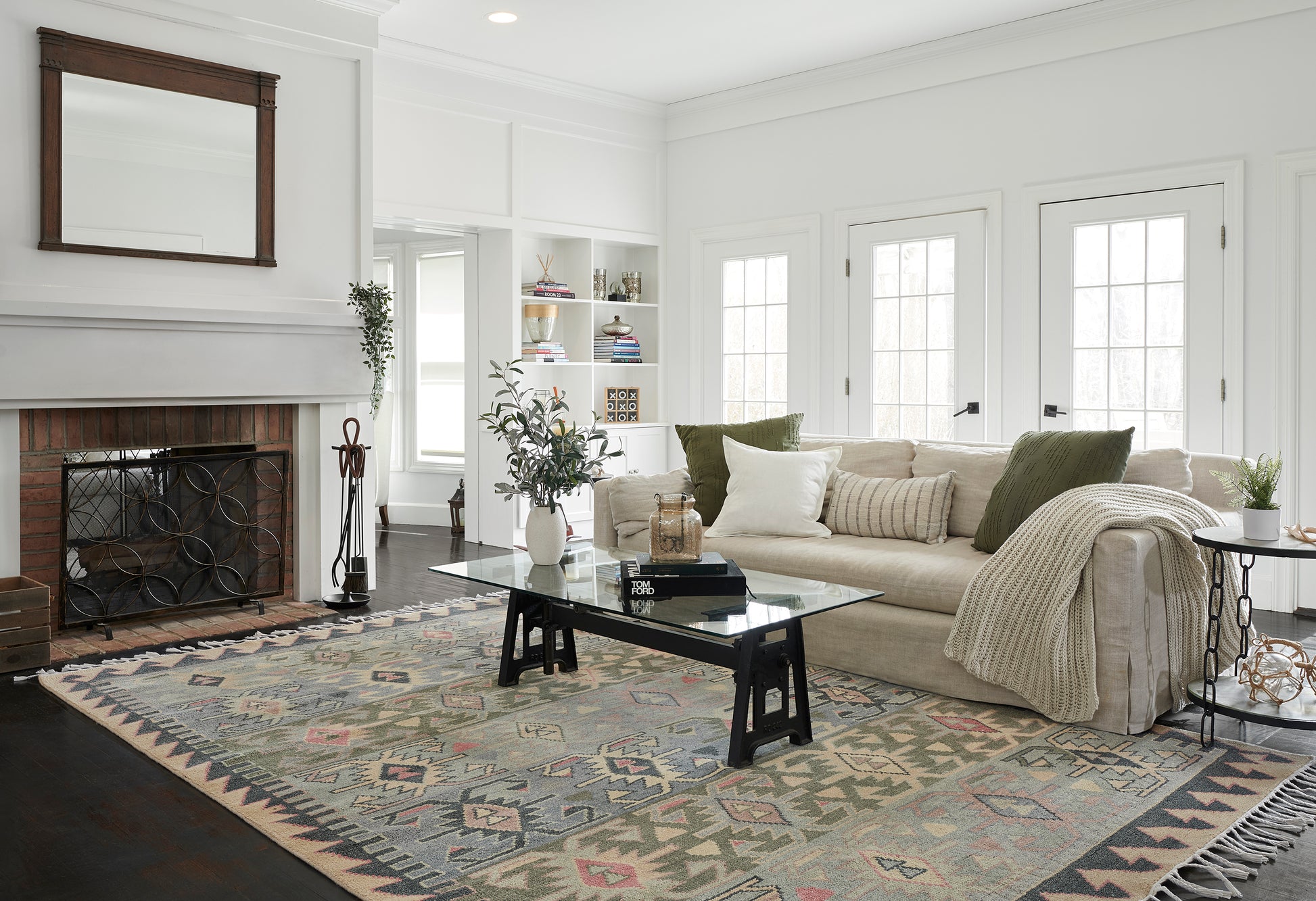 Geometric kilim area rug in blues, greens and pinks under a glass coffee table in a beige living room.