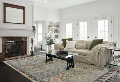 Geometric kilim area rug in blues, greens and pinks under a glass coffee table in a beige living room.
