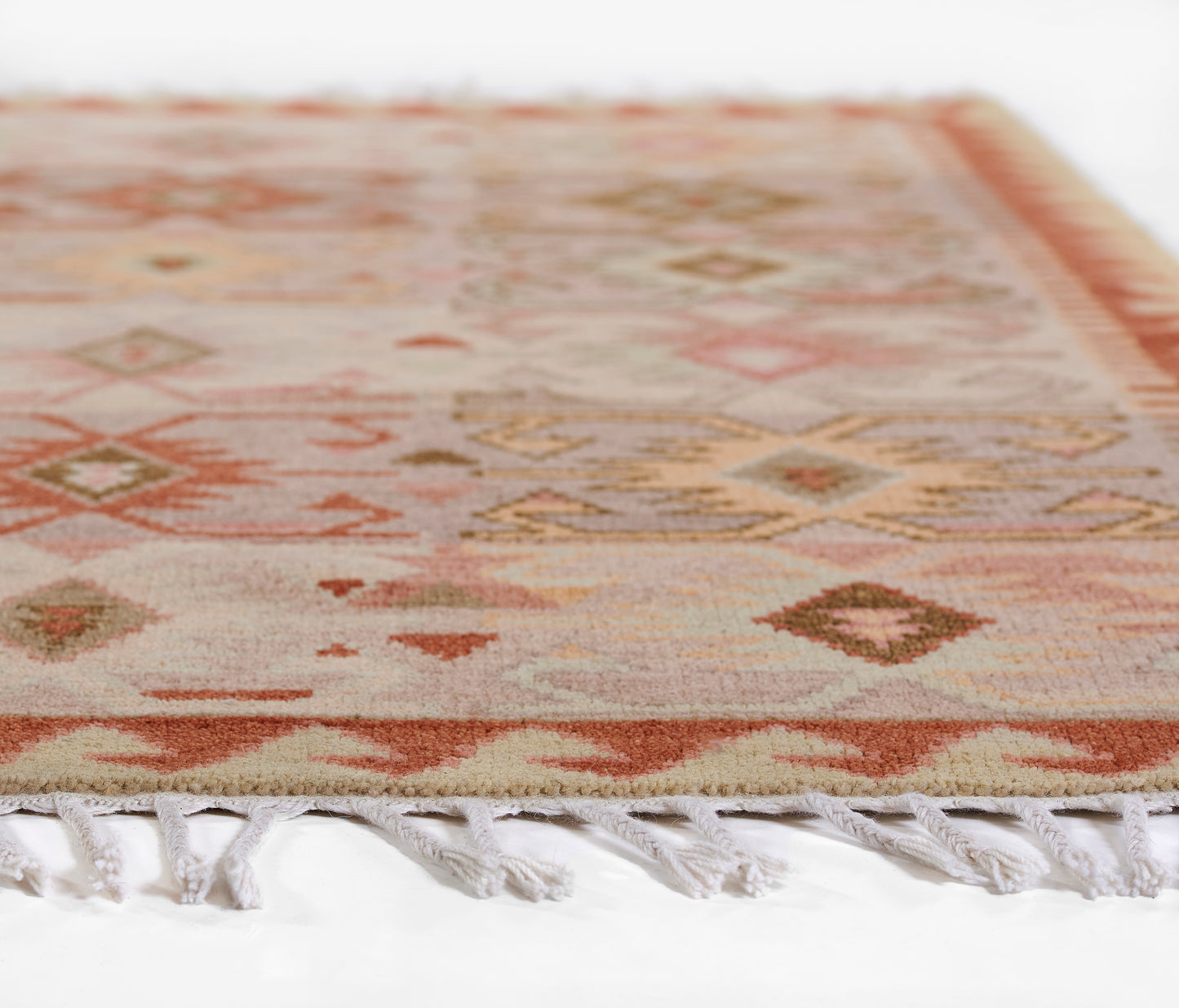 Geometric rug with diamond motifs in peach, pink, ivory and gold; fringed edge.