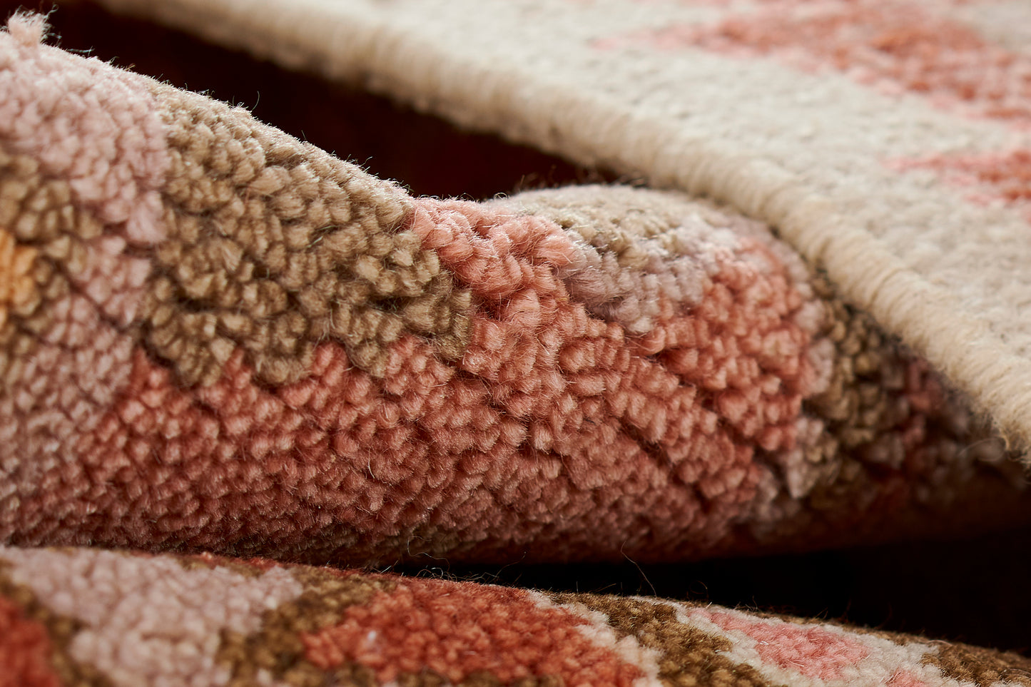 Close-up of a pink and coral rug with dense loop pile and beige border.